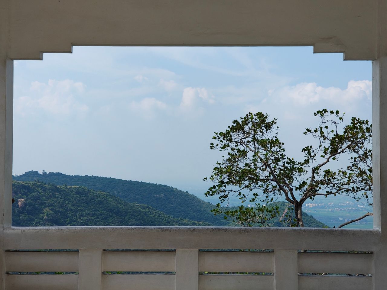 Framed view of distant hills and a tree from a balcony under a clear blue sky.