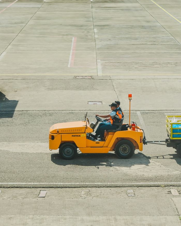 An airport ground vehicle towing luggage on the apron on a sunny day.